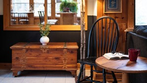 A cozy room with a wooden bench, a chair, a table with a red mug and glasses, and a lamp with animal designs. - New to VRBO Bumble Bear Inn in Bolton Landing (Bolton Landing)