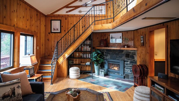 A wooden interior with a fireplace, bookshelves, a staircase, and a television. - New to VRBO Bumble Bear Inn in Bolton Landing (Bolton Landing)