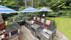 An outdoor patio with a grill, seating area, and umbrellas. - New to VRBO Bumble Bear Inn in Bolton Landing (Bolton Landing)
