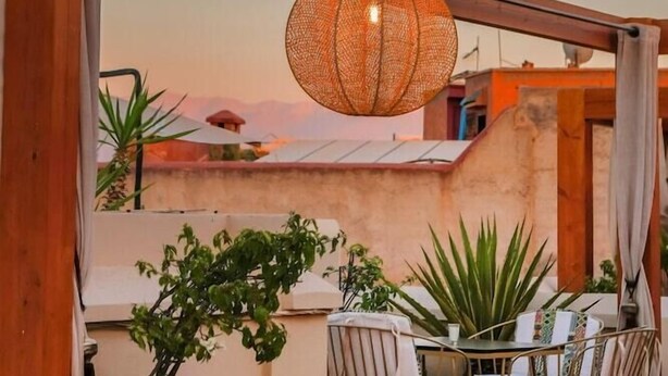 A wooden pergola with a woven light fixture, a table with chairs, and potted plants. - Riad Tahili (Marrakech)