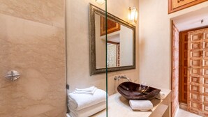 Un bany amb una paret de marbre, un envàs de dutxa de vidre, un lavabo amb un vàter fosc i una porta de fusta.