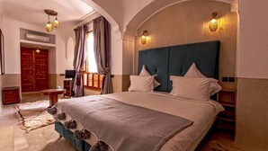 A large bed with a headboard, a wooden side table, and a rug. - Riad Tahili (Marrakech)