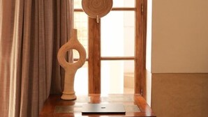 A room with a wooden table, a chair, a window with curtains, and a wooden sculpture. - Riad Tahili (Marrakech)