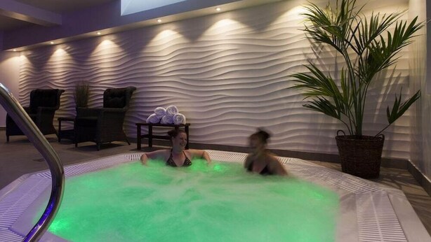 Ett spaområde med ett bubbelbad, solstolar och en vägg med en intressant yta.