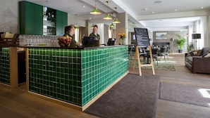 En hotellobby med en receptionsdisk klädd i gröna plattor, en bardisk och en sittgrupp med en soffa och stolar.