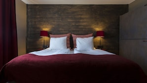 Ett hotellrum med en sänggavel i trä, två sänglampor, ett rött överkast och vita sängkläder.