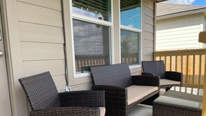 Un patio cubierto con mobiliario de mimbre, que incluye un sofá y dos sillones, además de una mesa de vidrio.