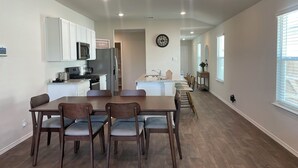 Una cocina moderna con armarios blancos, un refrigerador de acero inoxidable y un microondas. Hay un comedor con una mesa y sillas de madera.