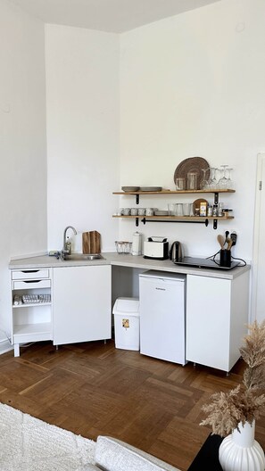 A compact kitchen with white cabinetry, a built-in dishwasher, and a countertop with various kitchen items.
