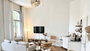 Una sala de estar moderna con un sofá, una mesa de comedor con sillas, un televisor y una zona de cocina con estanterías.