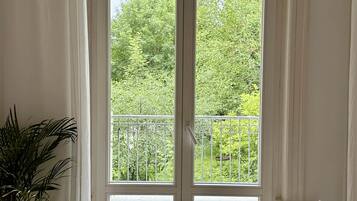 Ein Zimmer mit einem großen Glasfenster, das auf einen Balkon führt, einer Topfpflanze und einem grauen Sofa.