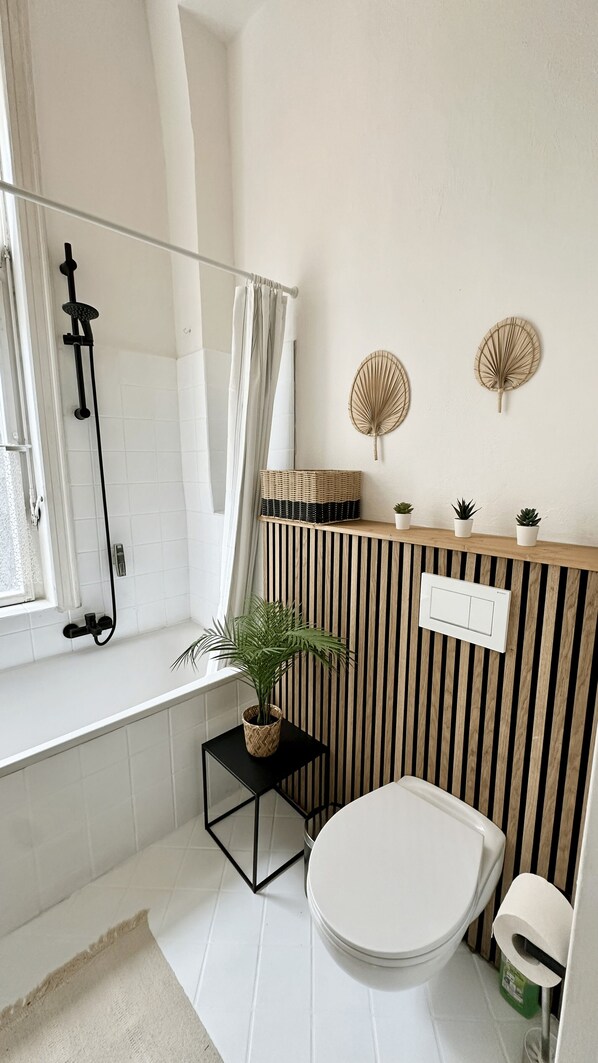 A modern bathroom with a shower, toilet, and a small shelf with plants.