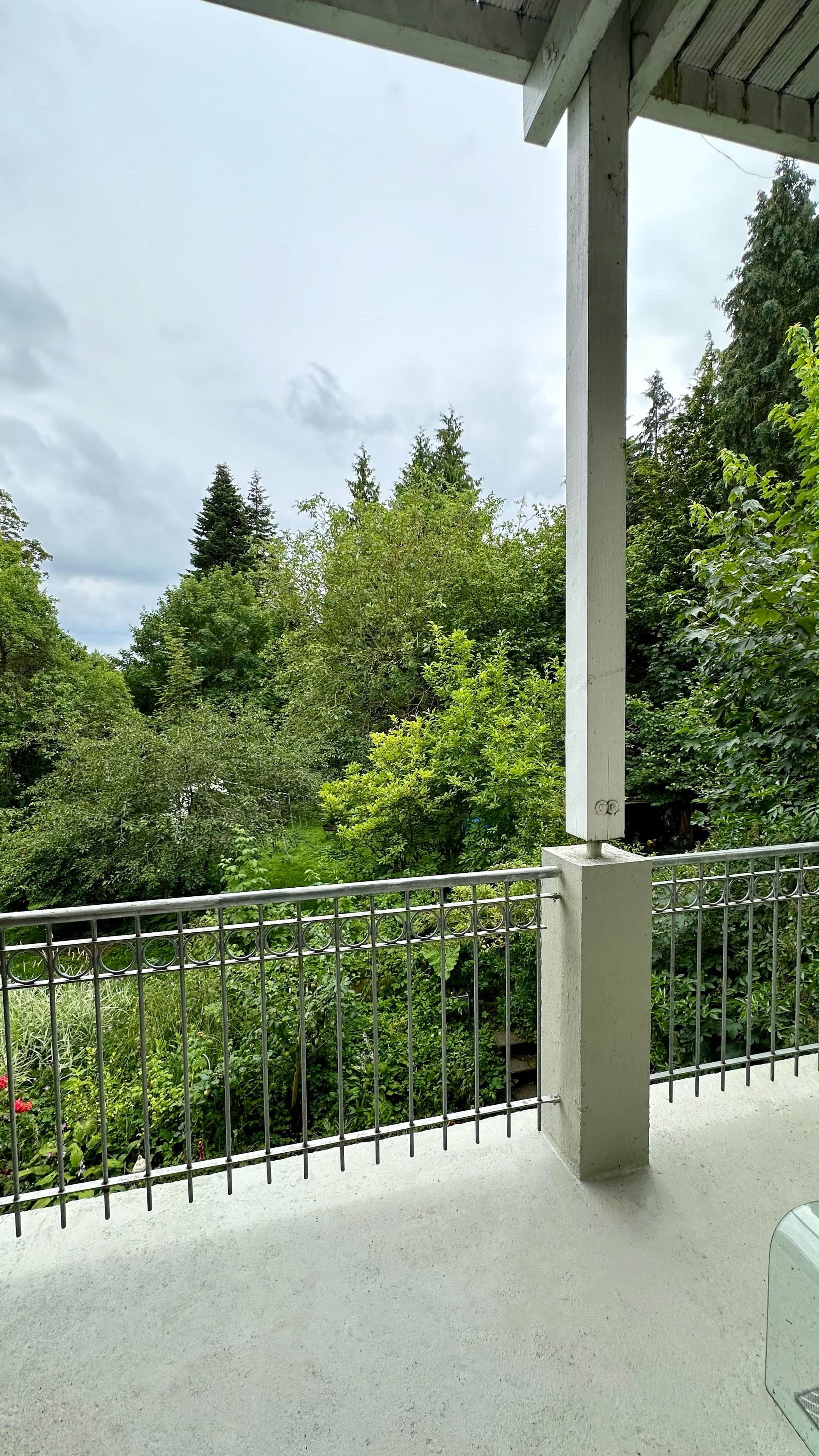 Un balcon doté d’une rambarde en métal, donnant sur un jardin luxuriant où poussent différentes espèces d’arbres et d’arbustes.
