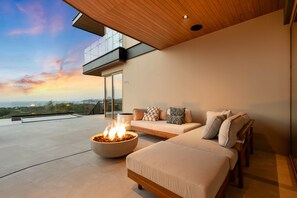 A modern outdoor seating area with a fire feature, a sofa, and a view of the landscape.