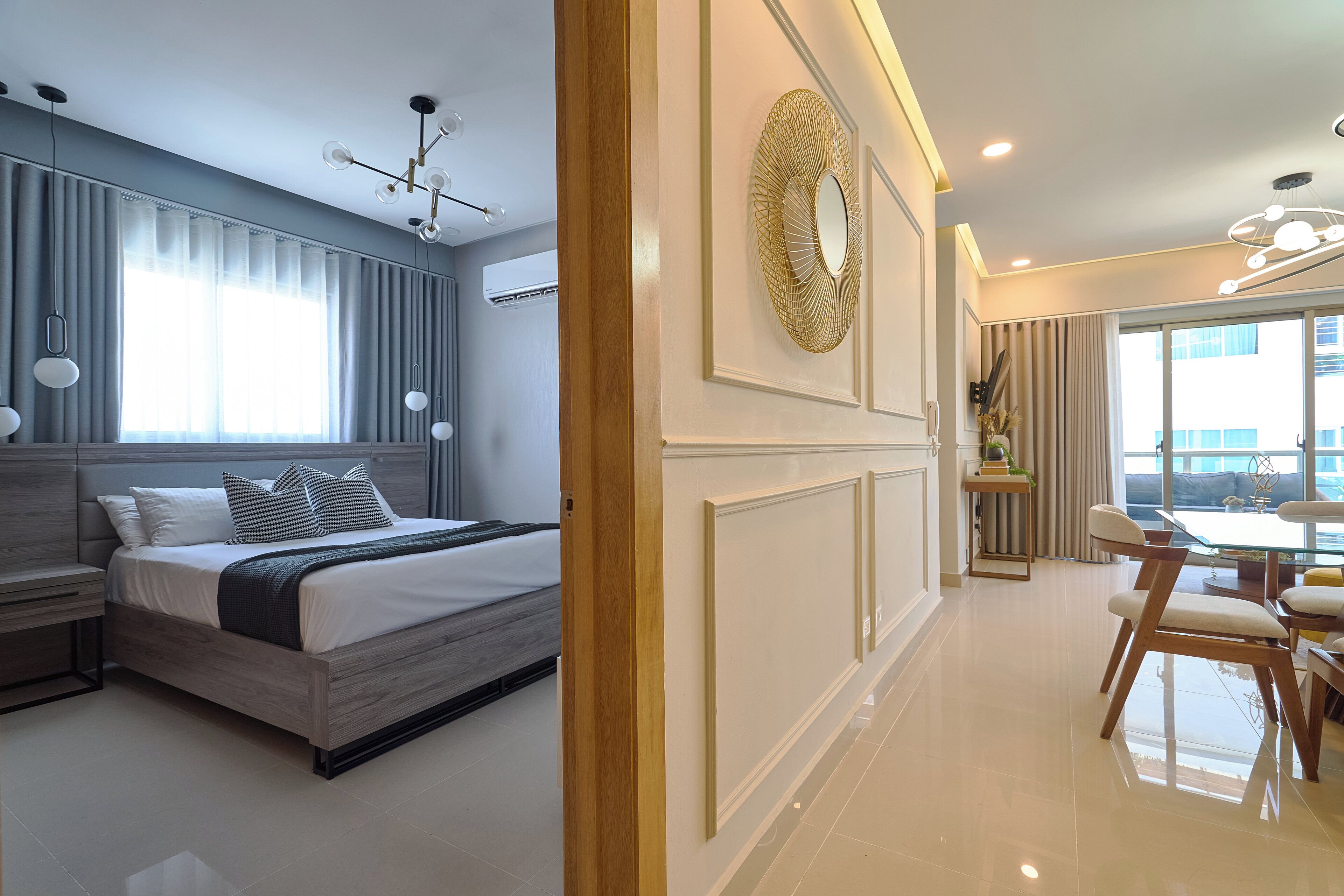 A modern hotel room with a large bed, a dining area with a table and chairs, and a large window with curtains.