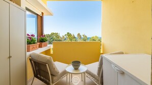 En balkon med et hvidt bord, to stole og et hvidt skab. Der er plantede planter på vindueskarmen.
