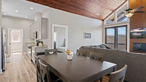 Eine moderne Küche mit weißen Schränken, ein Essbereich mit einem dunklen Holztisch und ein graues Sofa.