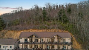 Ein mehrstöckiges Hotel mit einem Balkon im zweiten Stock, umgeben von bewaldeten Hügeln.