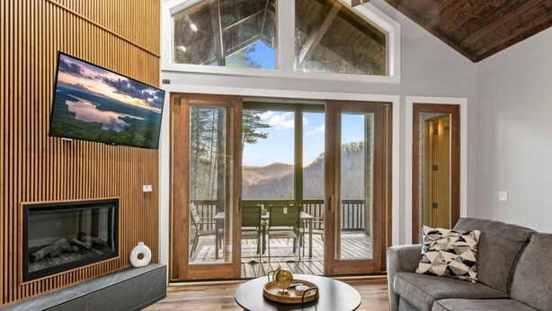 A modern living room with a fireplace, a flat-screen TV, a sofa, and a dining area with outdoor seating.