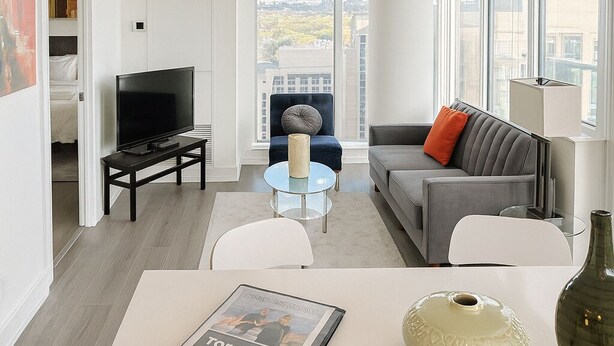 A modern living room with a sofa, a TV, a coffee table, and a dining area with a book and a vase.