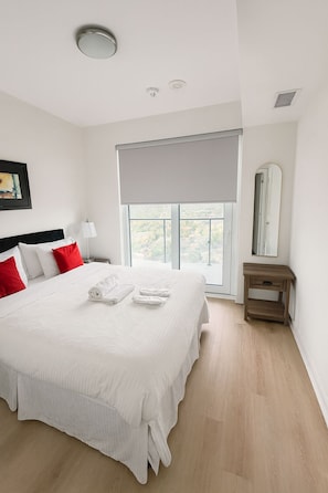 Quarto bem arrumado com uma cama grande, mesa de cabeceira, janela com vista e um espelho.