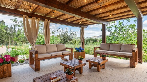An outdoor patio with wooden furniture, including sofas and tables, surrounded by potted plants and a view of greenery. - House Adele - Dreaming Vacation (Villa San Pietro)