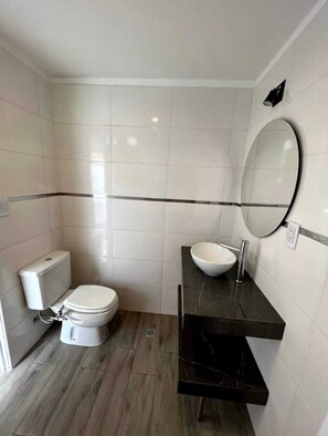 A small, modern bathroom with white tiles, a toilet, a sink with a mirror, and a black countertop.
