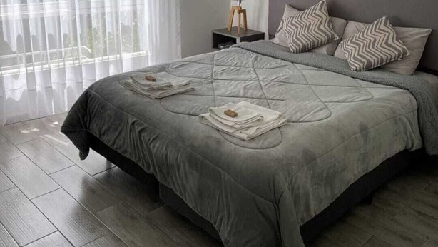 Une chambre moderne avec un grand lit, une table de chevet avec une lampe et des rideaux légers.