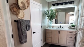 A bathroom with a large mirror, a sink, and a toilet. There is a towel rack with towels and a decorative wall hanging. - Luxury Riverfront Home in Parker - Private Dock, Mini Pool & Game Room (Parker)