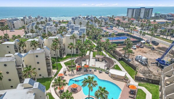 Un hotel frente al mar con varias edificaciones, una piscina y palmeras.
