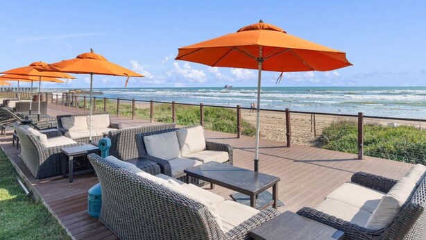 Una terrazza sul mare con mobili in vimini e ombrelloni arancioni, con vista sull'oceano.