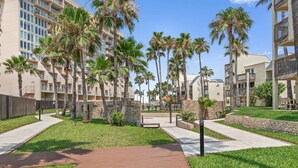 Un hotel moderno con diversi piani, palme e un'area verde curata.