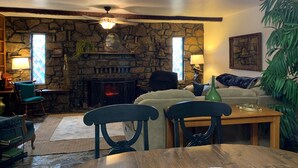 A cozy living room with a stone fireplace, wooden furniture, and a large plant. - Charming 3-bedroom house with WiFi, AC in delightful Yellville (Yellville)