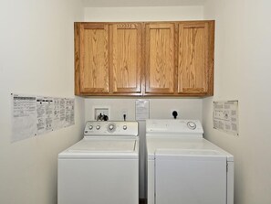 A laundry room with two stacked washers and dryers, wooden cabinets above, and laundry instructions on the walls.
