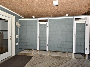 A row of four individual bathroom stalls with a wooden ceiling and a gray wall.