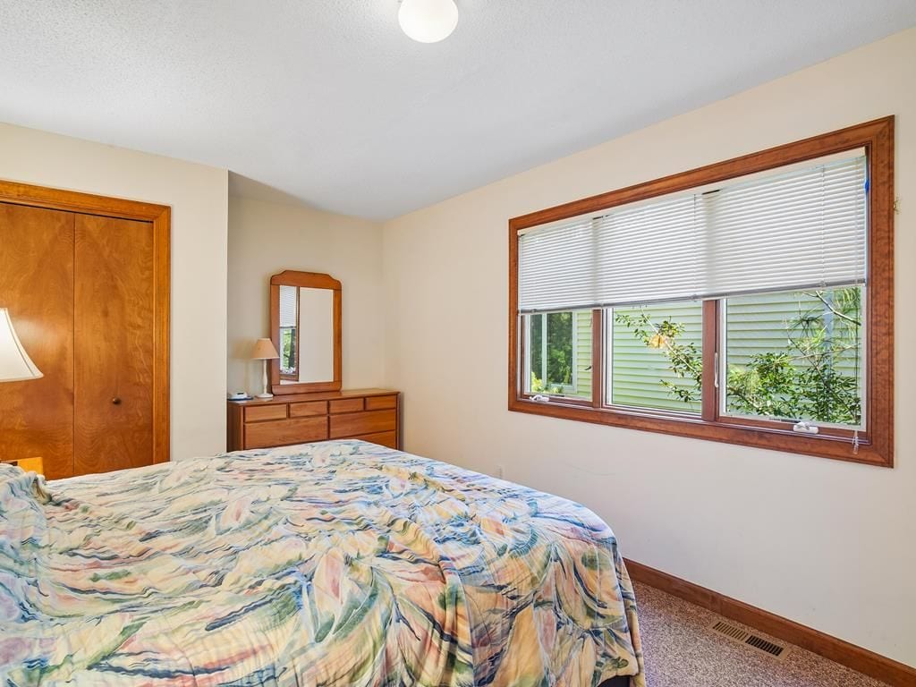 A bedroom with a bed, a dresser, a mirror, and a window with blinds.