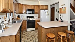 Una cocina con armarios de madera, microondas, refrigerador, estufa y una barra con taburetes.