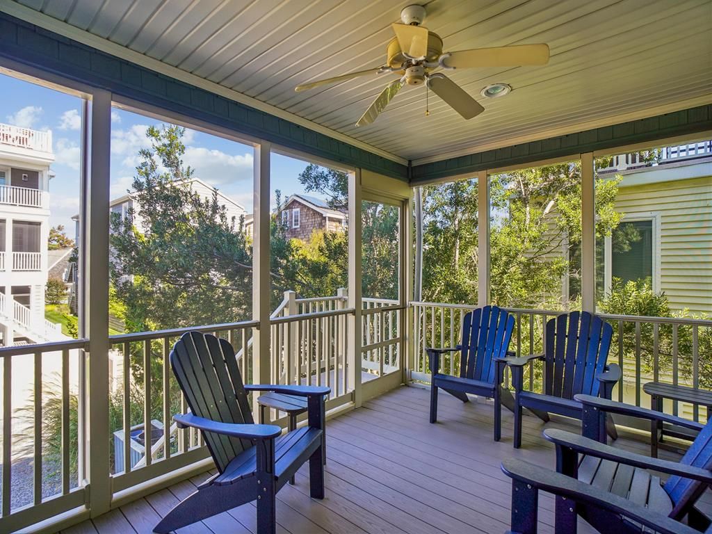 A covered porch with wooden flooring, a ceiling fan, and several Adirondack chairs.