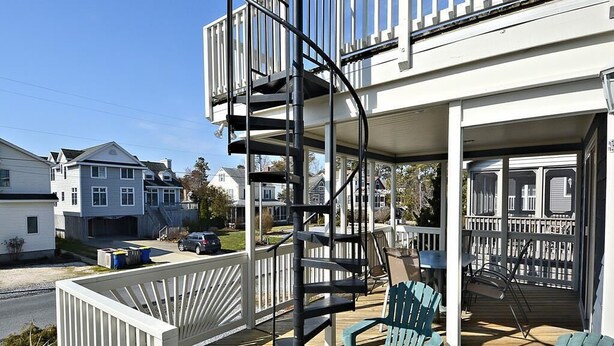 A residential building with a covered porch, outdoor seating, and a spiral staircase.