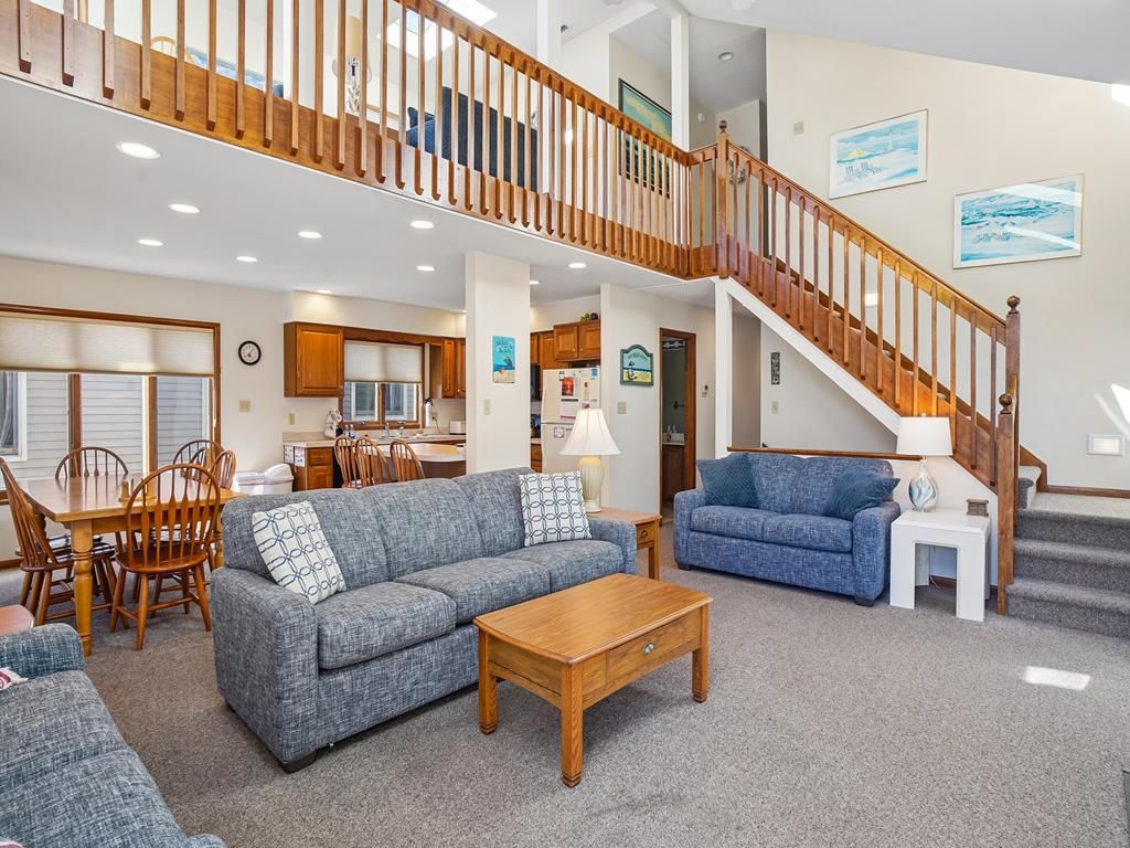 A spacious living area with a staircase, a dining table, and a kitchen in the background.