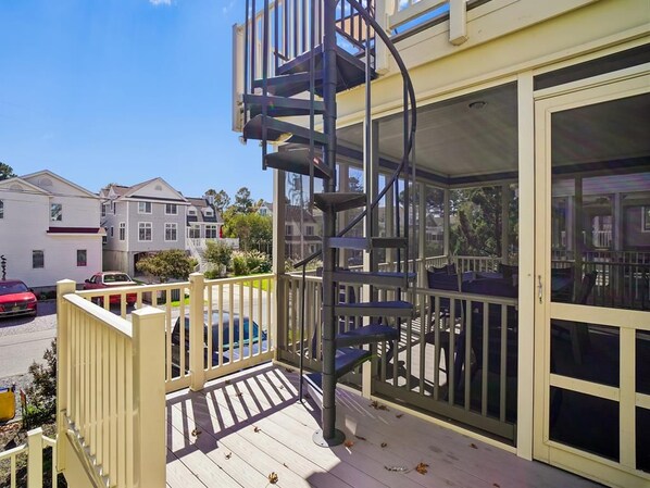 A residential property with a spiral staircase leading to a balcony, a covered outdoor seating area, and a view of neighboring houses.