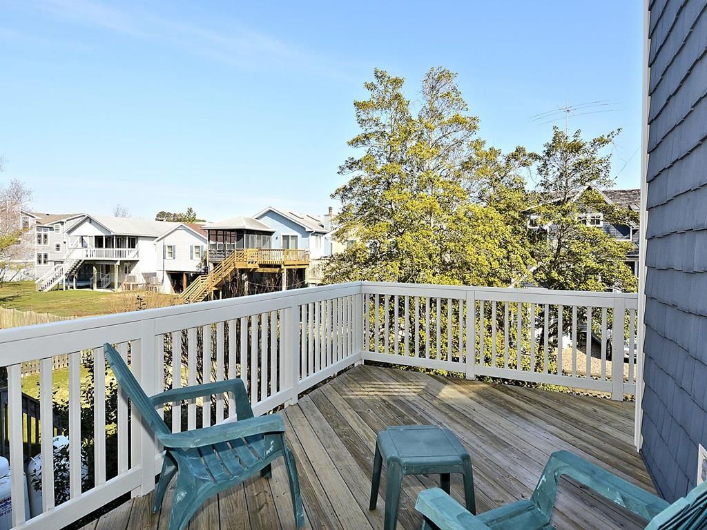 A wooden deck with a white railing, green plastic chairs, and a view of houses and trees.