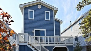 A two-story house with a blue exterior, white trim, and a wooden deck with a white railing.