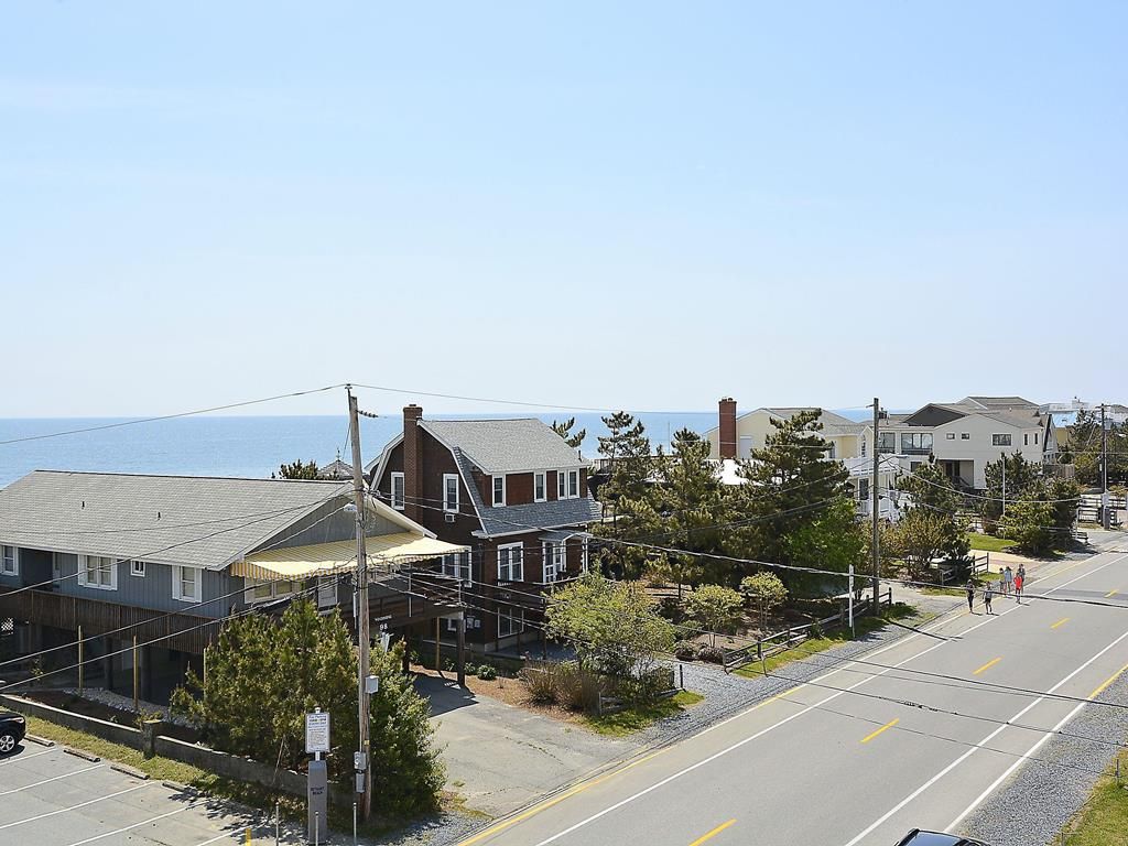 A residential street with houses, a clear sky, and a view of the ocean.