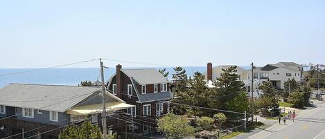 A residential street with houses, a clear sky, and a view of the ocean.