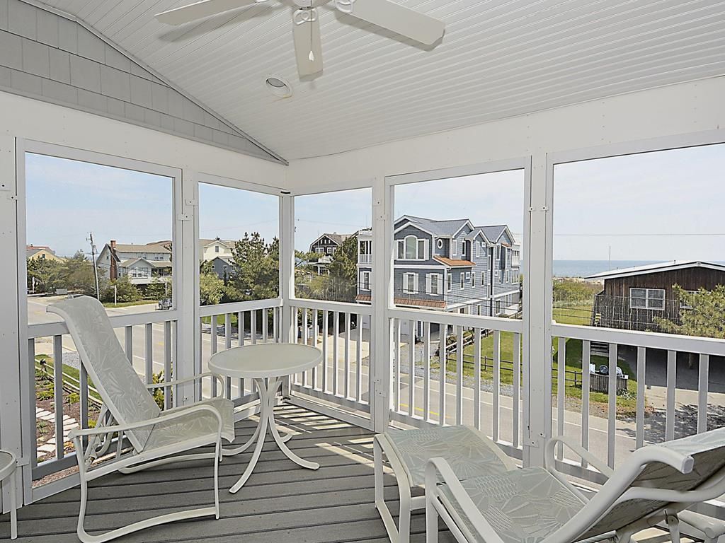 A covered porch with white furniture and a view of houses.