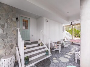 A porch with a stone wall, a green door, white railings, and outdoor seating.