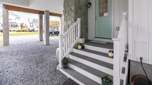 Un porche con muro de piedra, puerta color turquesa y escalera adornada con plantas en macetas.