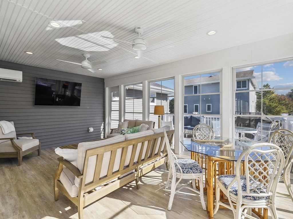 A sunlit room with a wooden bench, white chairs, and a glass table.