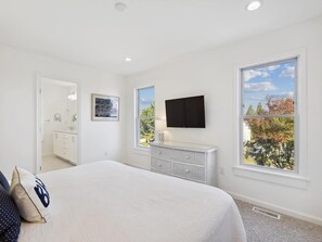 A bedroom with a bed, a dresser, a television, and a window with a view of trees.